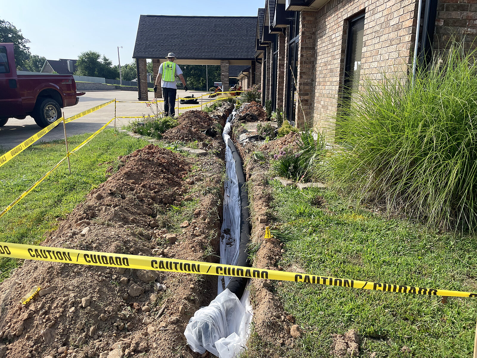 Narrow french drain trench with perforated pipe alongside a commercial building